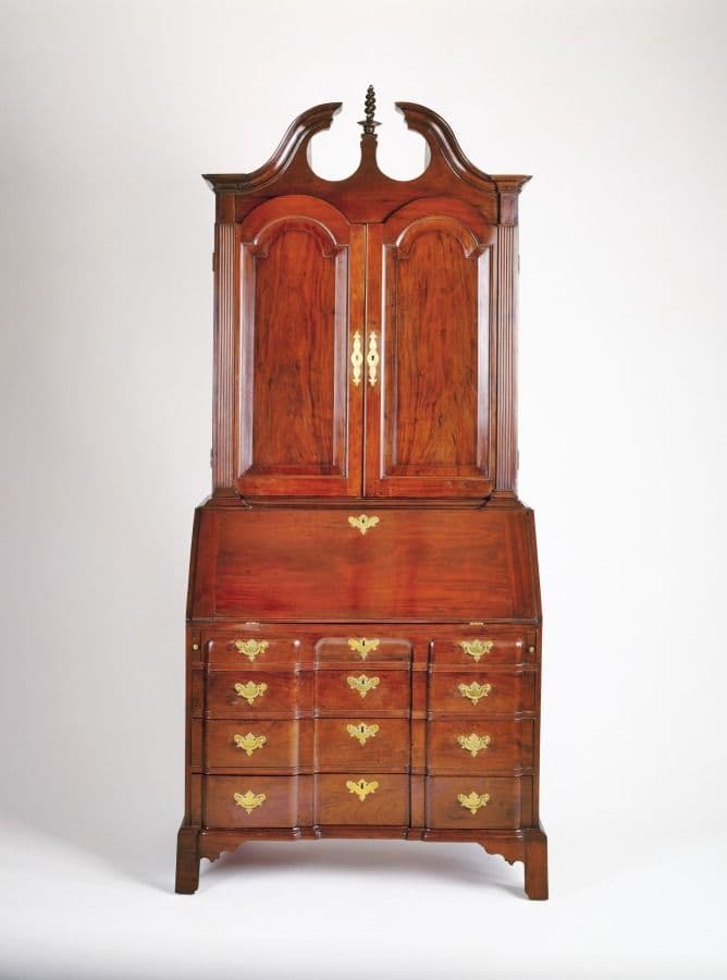 Tall mahogany desk and bookcase with slant-front desk, paneled doors and a pediment with finials