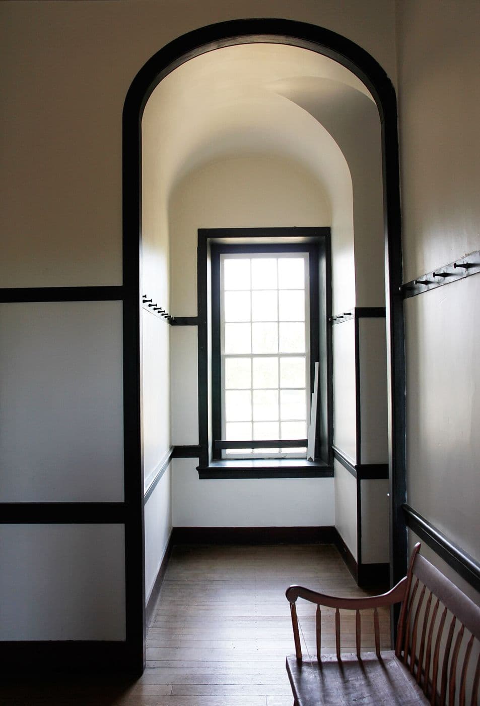 White Shaker hallway with an arched ceiling, dark wood peg rail and a bench under a window