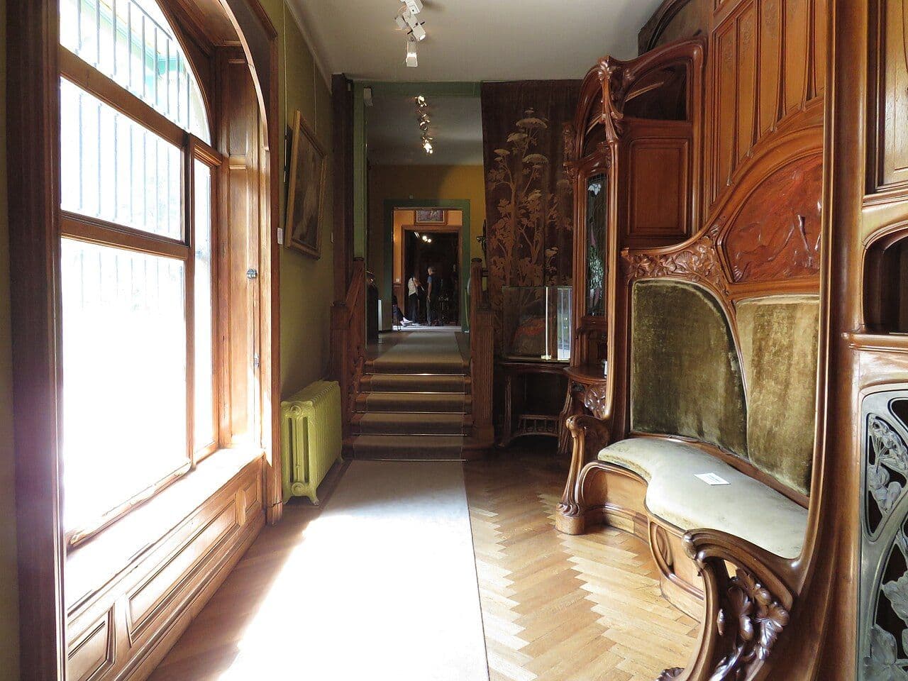 Art Nouveau room with carved wooden built-in seating, screen and a stair