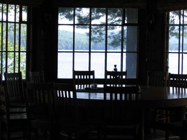 Dark log-and-timber dining hall with large windows overlooking a lake