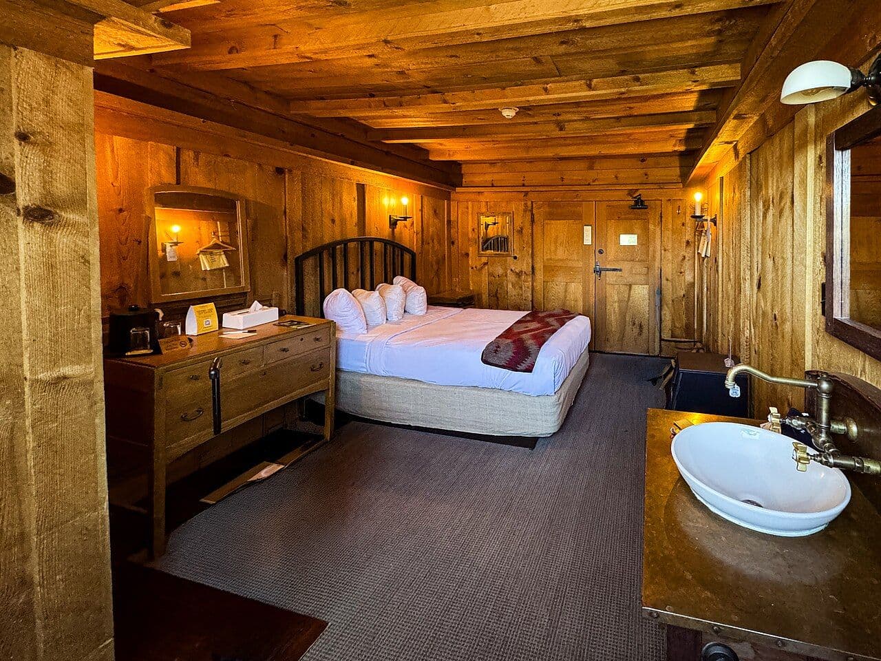 Rustic guest room with exposed log walls and ceiling, a wooden bed and a washbasin
