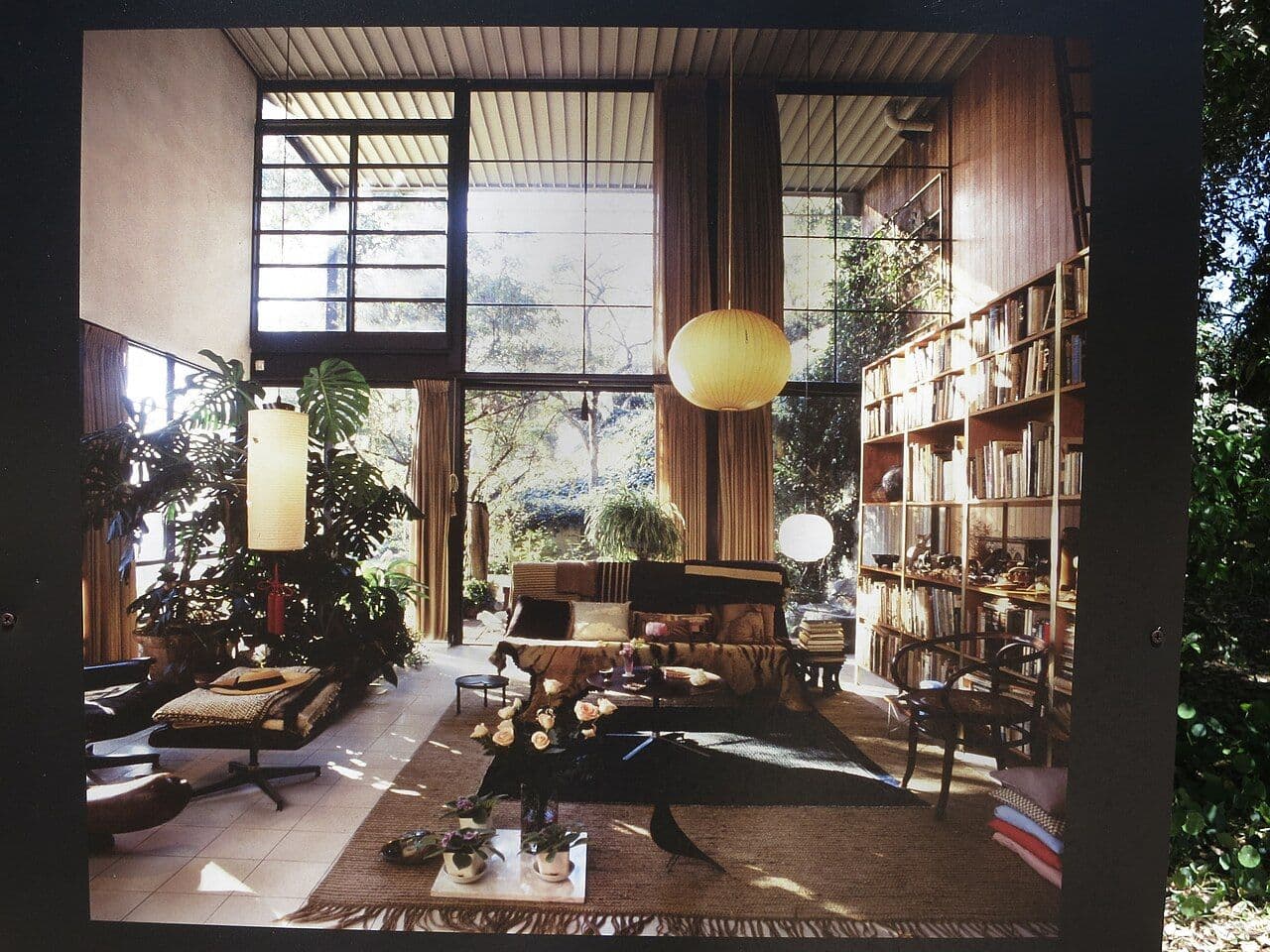 Double-height mid-century living room with open shelving, wood paneling and tall windows
