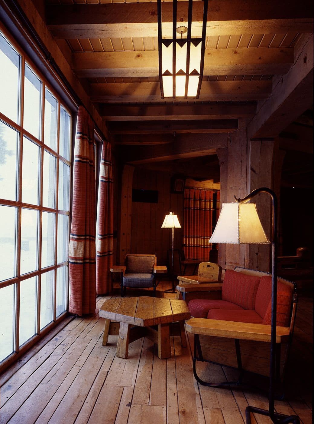 Warm wooden lodge interior with heavy timber framing, large windows and rustic furniture
