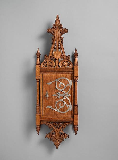Narrow oak wall cabinet with pointed Gothic cresting and decorative metal strapwork on the door