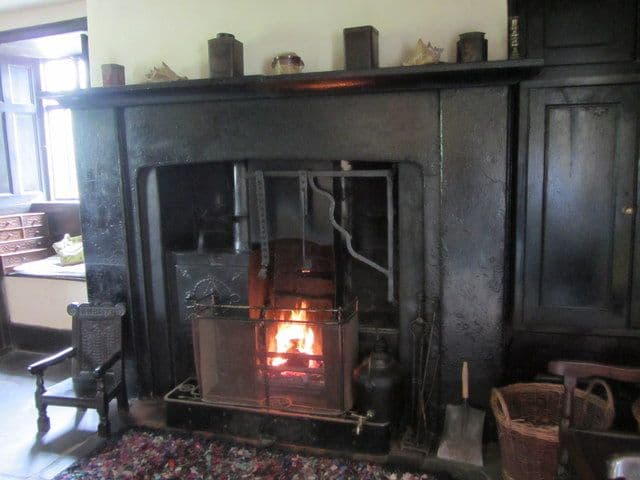 Wide farmhouse kitchen fireplace with a fire in a cast-iron range and dark woodwork