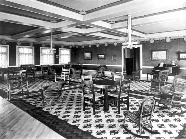 Historic photograph of a hotel lobby with a coffered beamed ceiling and rustic furniture