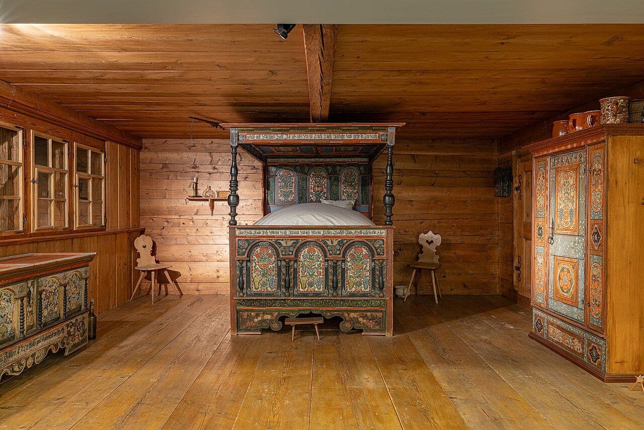 Swiss farmhouse room with painted folk-art cupboard, bed and chest against wood paneling