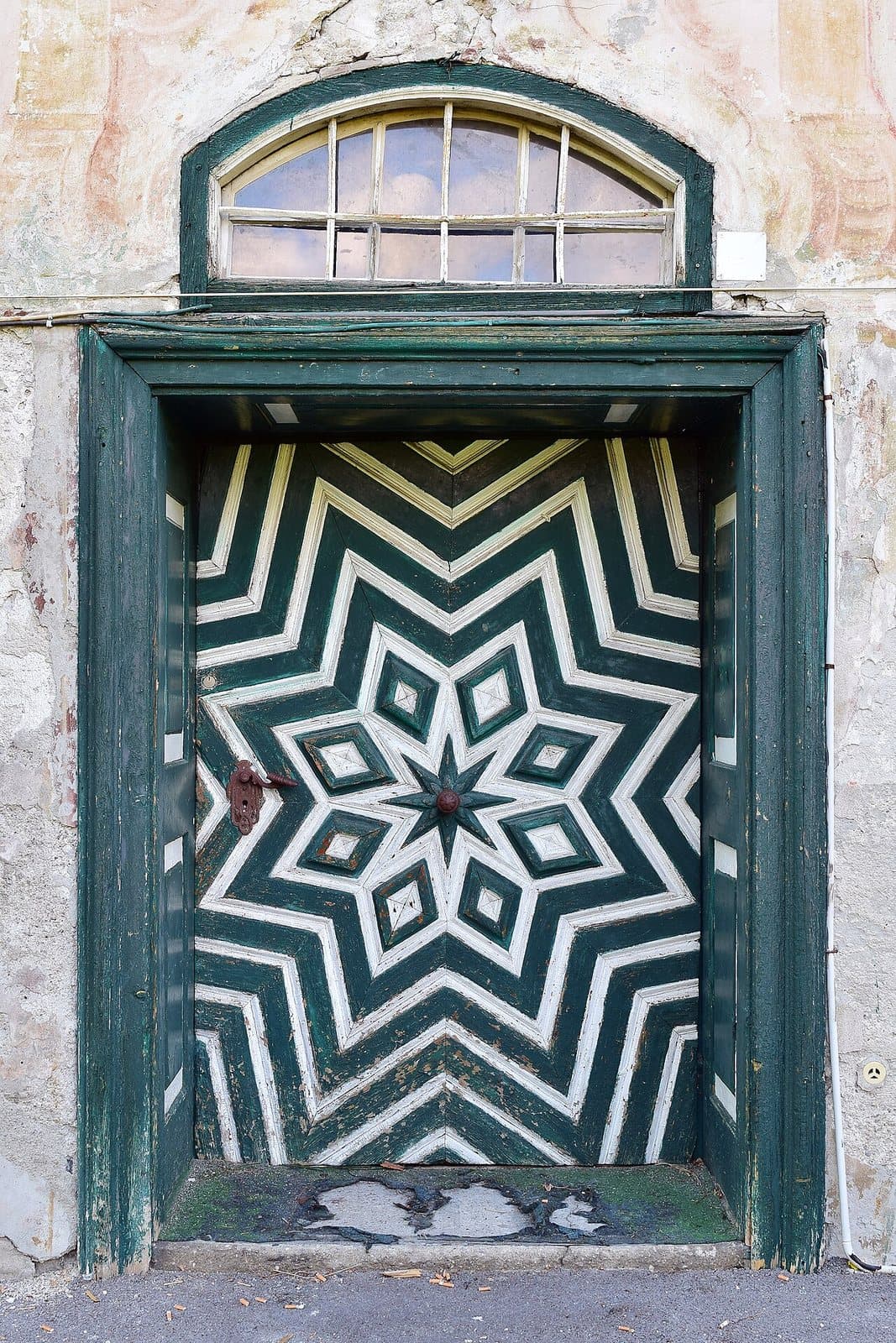 A door painted with a green and white eight-pointed star pattern radiating to the frame, under an arched fanlight