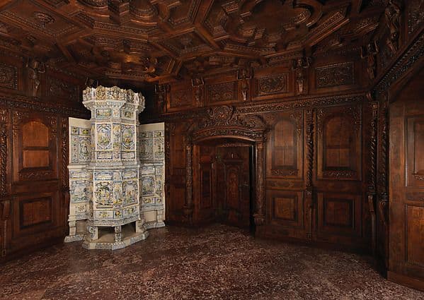 Swiss wood-paneled room with arched wall panels, a coffered ceiling and a tiled stove