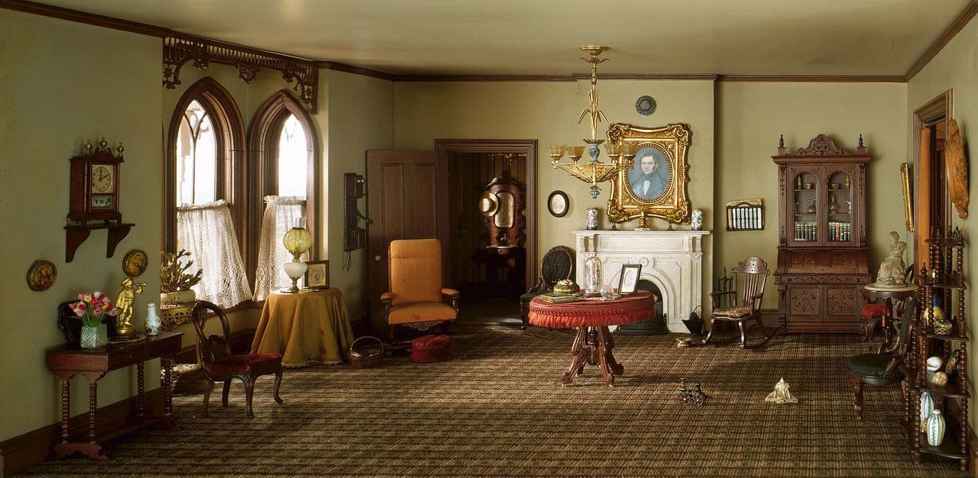 Miniature Victorian parlor with a white mantel, gilt mirror, tall secretary and patterned wallpaper